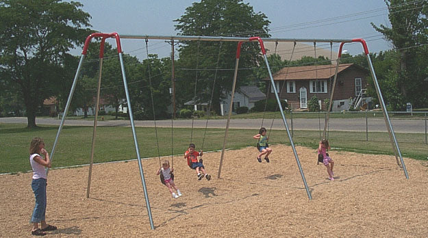 Metal tripod frame swing set with four children swinging on seats over wood chip ground in a neighborhood park