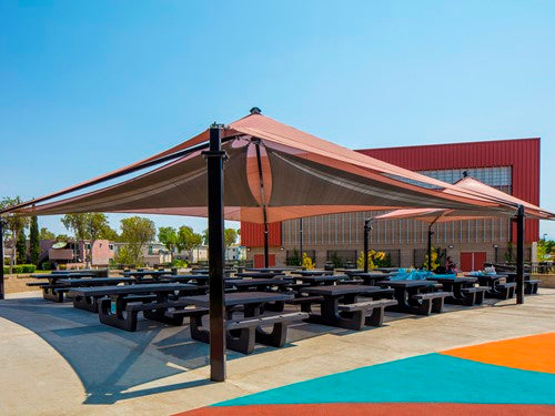 Modern outdoor shade structure with layered fabric canopies covering multiple picnic tables in a public park setting