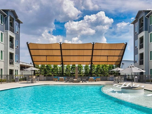 Slanted cantilever wing shade with tilted fabric top and two grey columns over outdoor pool seating area