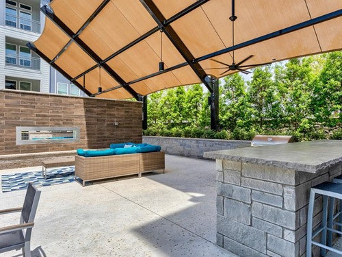 Outdoor seating with wicker sofa featuring blue cushions, stone fireplace, built-in grill, and cantilever wing cabled shade structure