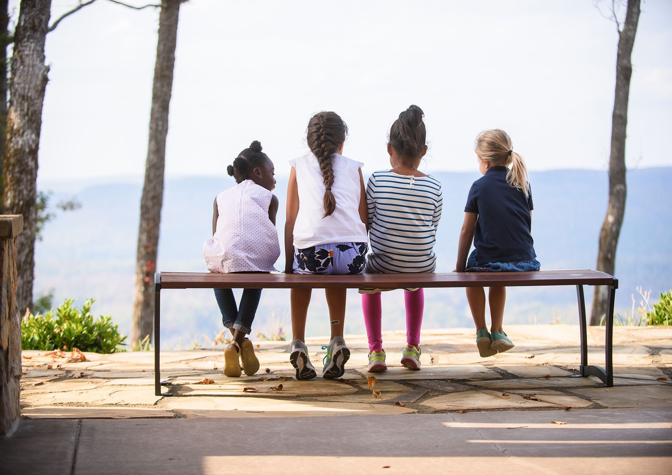 Four children seated on a sleek Ipe wood outdoor bench with steel end frames on a stone patio