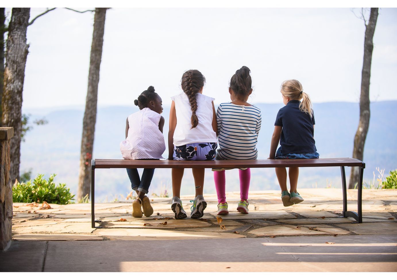Outdoor powder-coated steel bench without backrest with four children seated, natural landscape in background