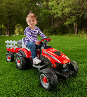 Child riding bright red toy tractor with detachable gray trailer on green grass outdoors