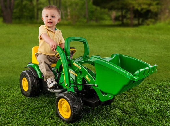 Young child seated on green and yellow ride-on loader with working front bucket on grass lawn