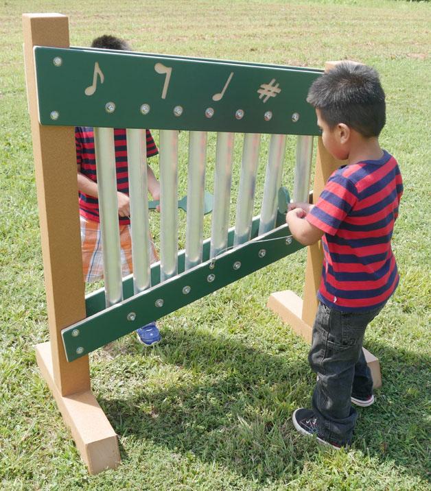 Child playing a colorful freestanding outdoor musical chime wall with metal bars and musical note panels
