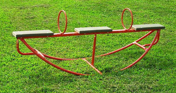 Red three-seat portable see saw with safety handlebars and stoppers on grass playground surface