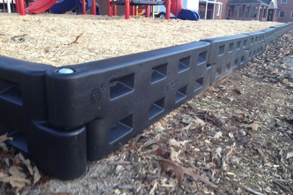 Black plastic playground border with integrated surfacing guide surrounding wood chip play area and playground equipment