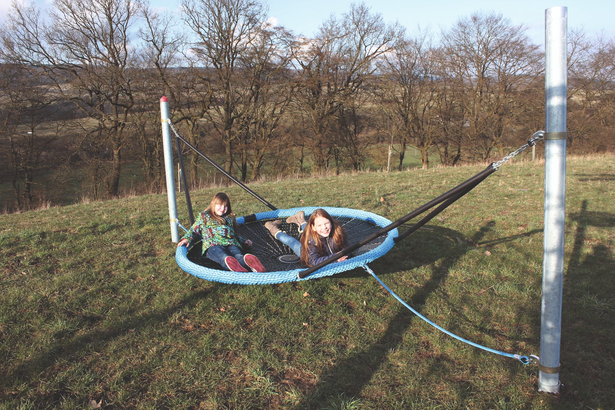 Two children relaxing on a blue and black netted bird's nest cradle swing on grass outdoors