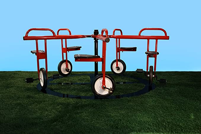 Red metal merry-go-round with five bike-style seats and pedals arranged on a circular track on grass.