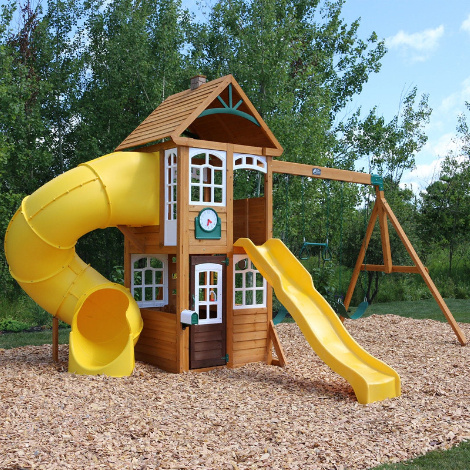 Lewiston Retreat Wooden Swing Set with two yellow slides, wooden clubhouse, swings, play clock, and acro bar on wood chip ground outdoors