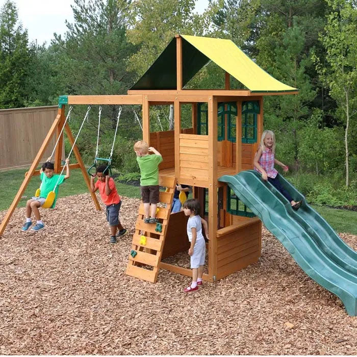 Wooden playset with yellow canopy, green double wave slide, rock climbing wall, two belt swings, and children playing outdoors