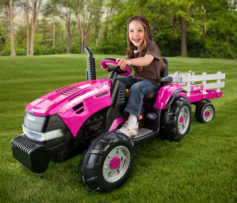 Child on pink 12-volt ride-on tractor with large detachable stake-side trailer on grass