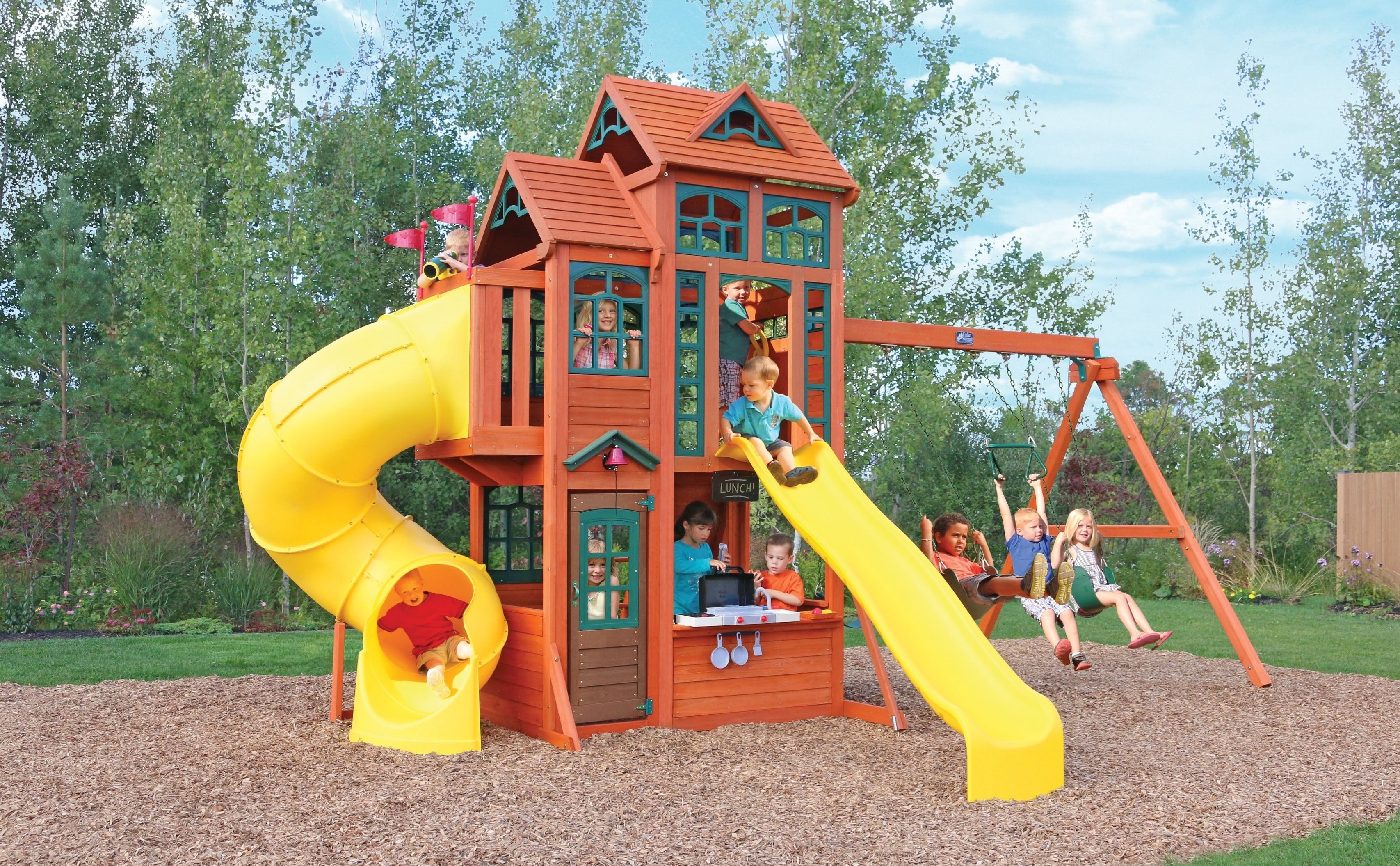 Canyon Ridge Wooden Swing Set with two yellow slides, wooden clubhouse, play kitchen, climbing rockwall, and swings outdoors