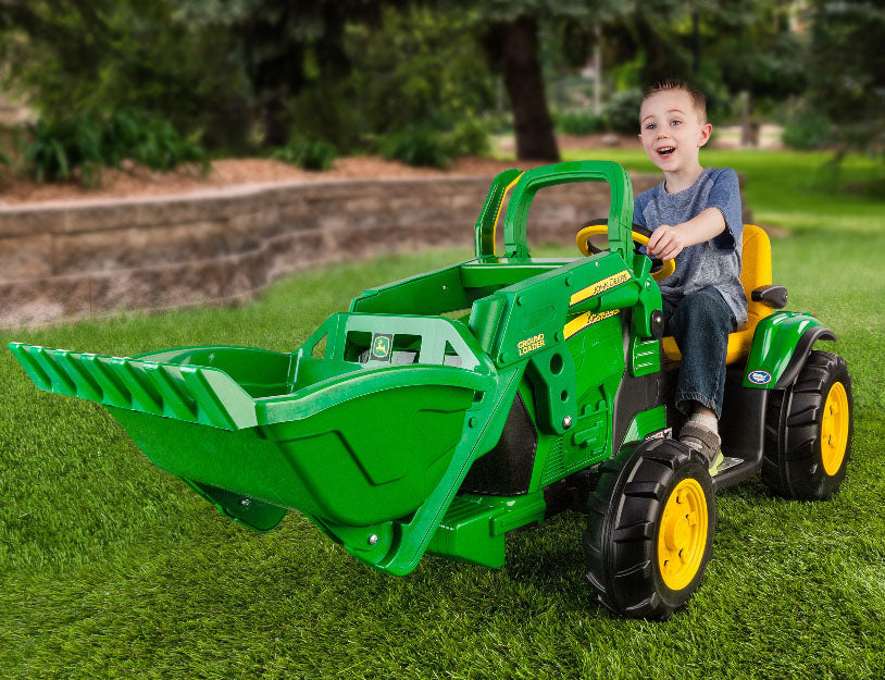 Child on green and yellow electric toy tractor with working front loader on grass