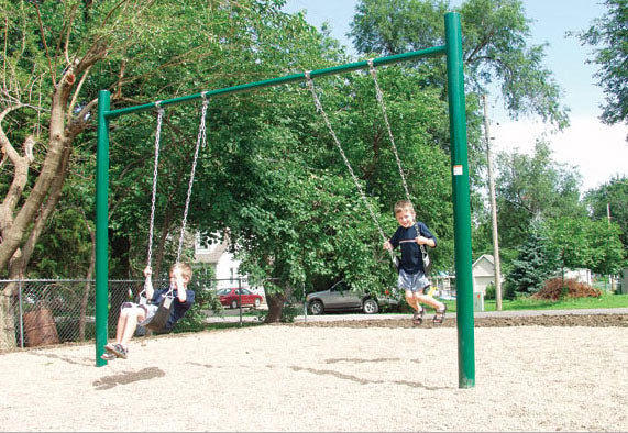 Green metal single post swing set with two children swinging on chains in an outdoor playground setting
