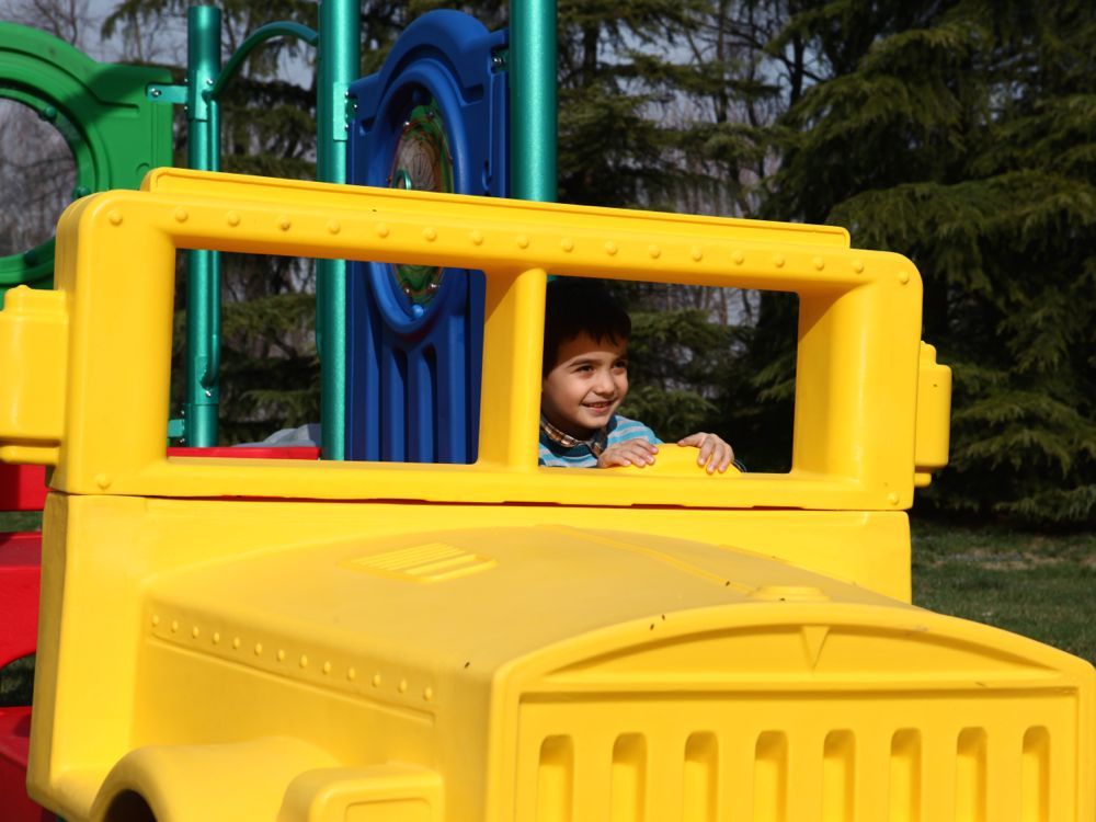 Child inside bright yellow plastic play truck with colorful playground equipment in the background