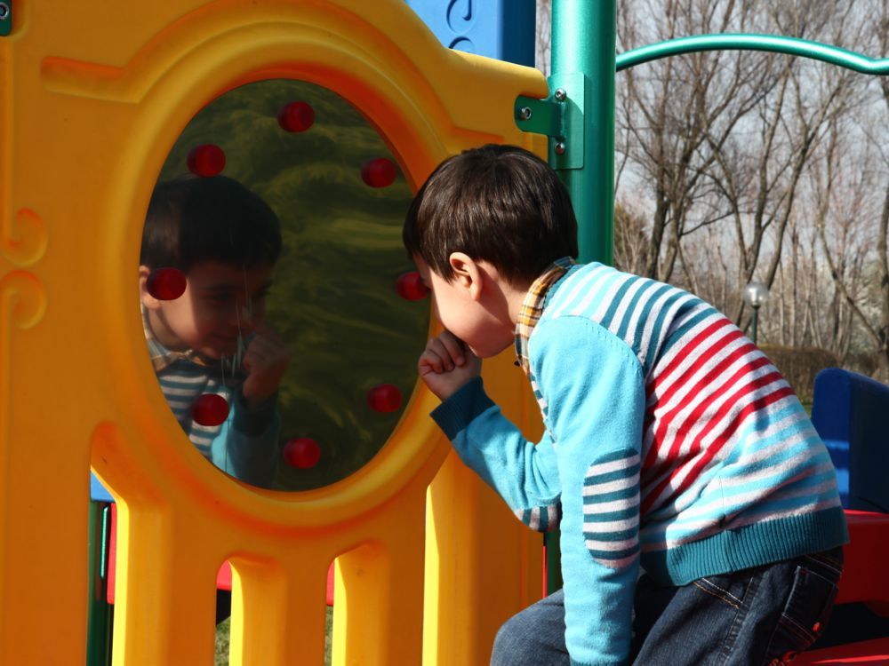 Young child in striped sweater engaging with reflective play panel on colorful outdoor playground structure