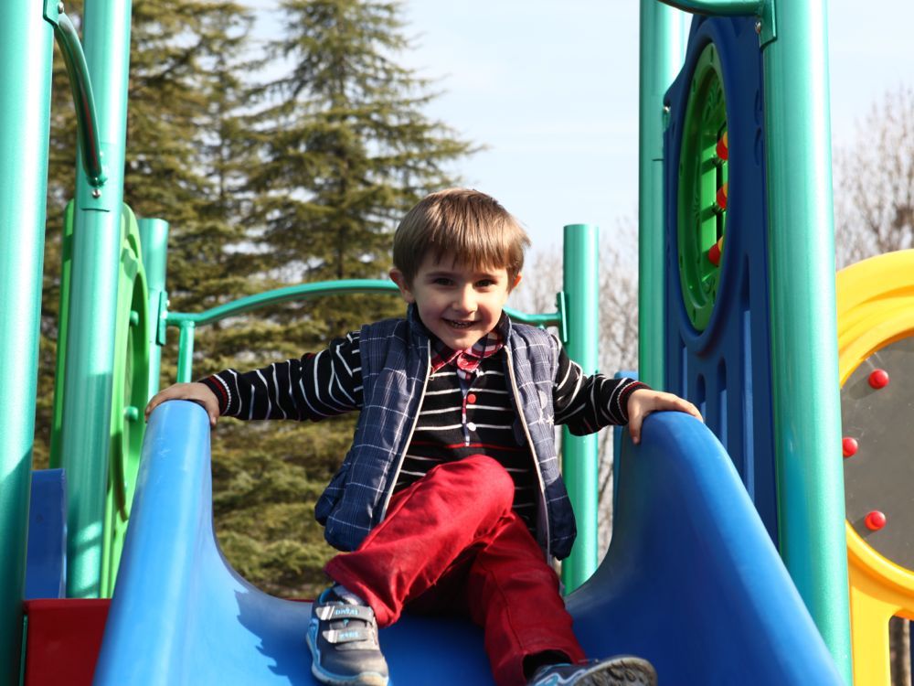 Young child sliding down blue slide on colorful early childhood playground with green and yellow play structures outdoors