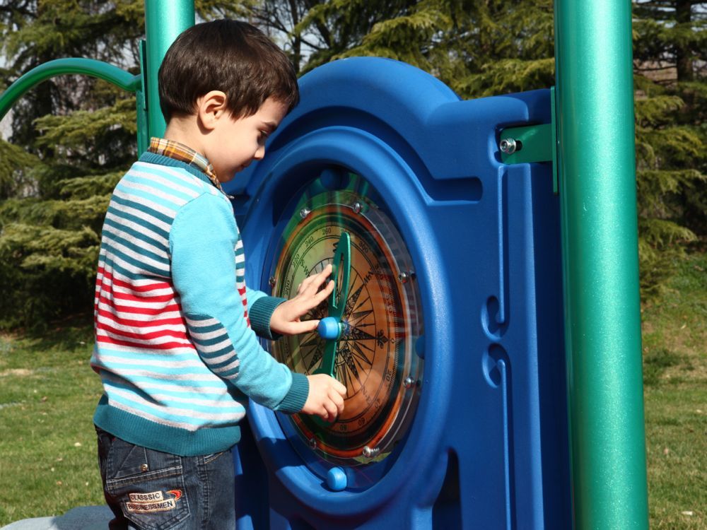 Young child engaging with a large blue compass panel on an outdoor explorer-themed playground playset