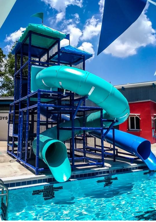 Three large curved blue and teal water slides with protective netting descending into a pool under a partly cloudy sky