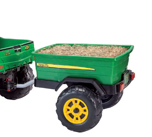 Green toy trailer with rugged yellow wheels attached to a children's riding vehicle, filled with straw-like material