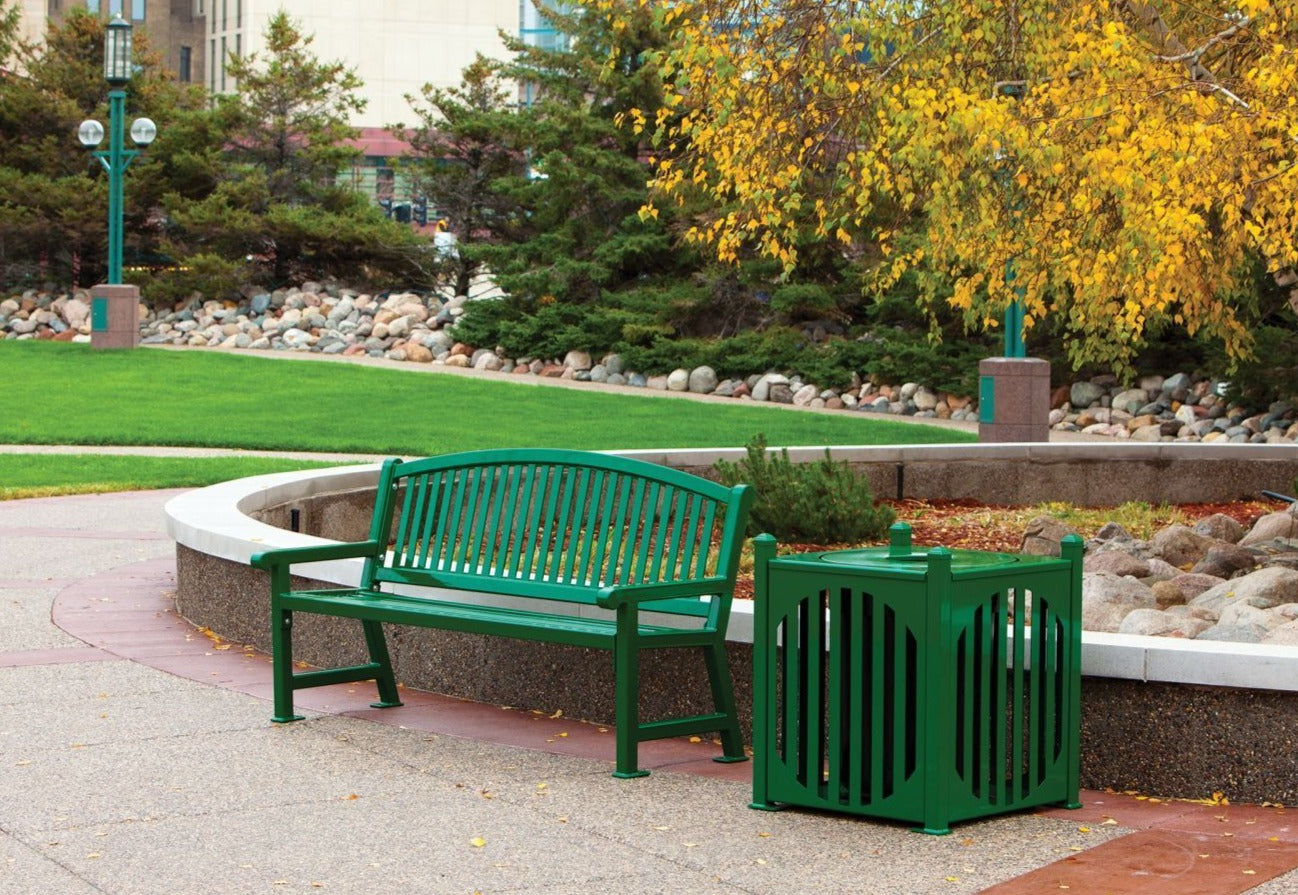 Green metal outdoor bench and matching square trash receptacle with vertical slats in landscaped park setting