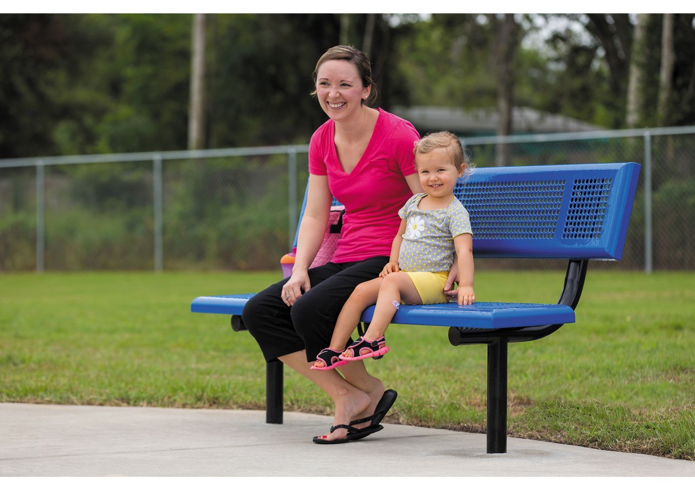 Blue perforated metal bench with backrest and black steel legs on concrete near grass outdoors