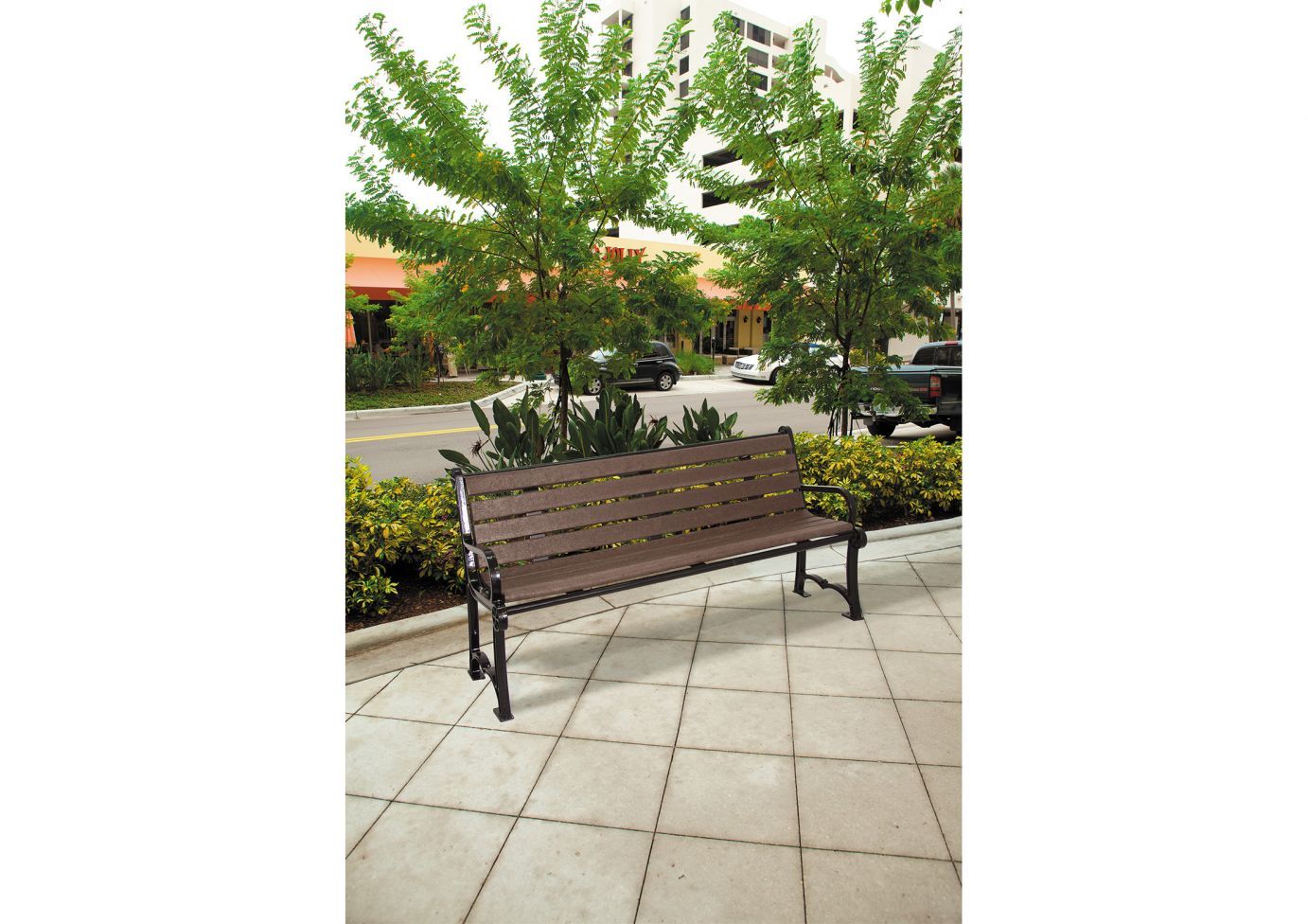 Outdoor bench with ornate aluminum frame and recycled planks on tiled patio near green shrubs and trees