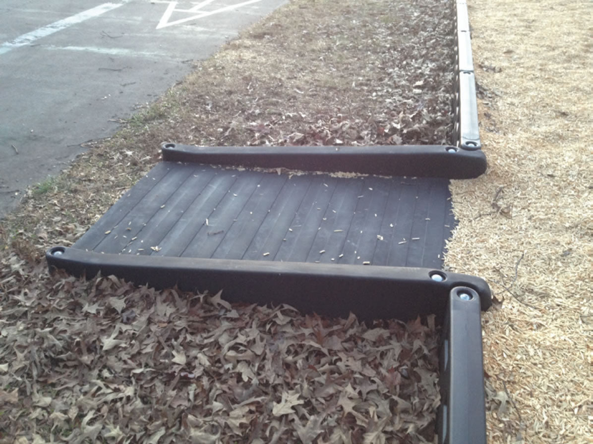 Black textured ADA accessible half ramp with raised edges, bordered by mulch and wood chips in outdoor playground.