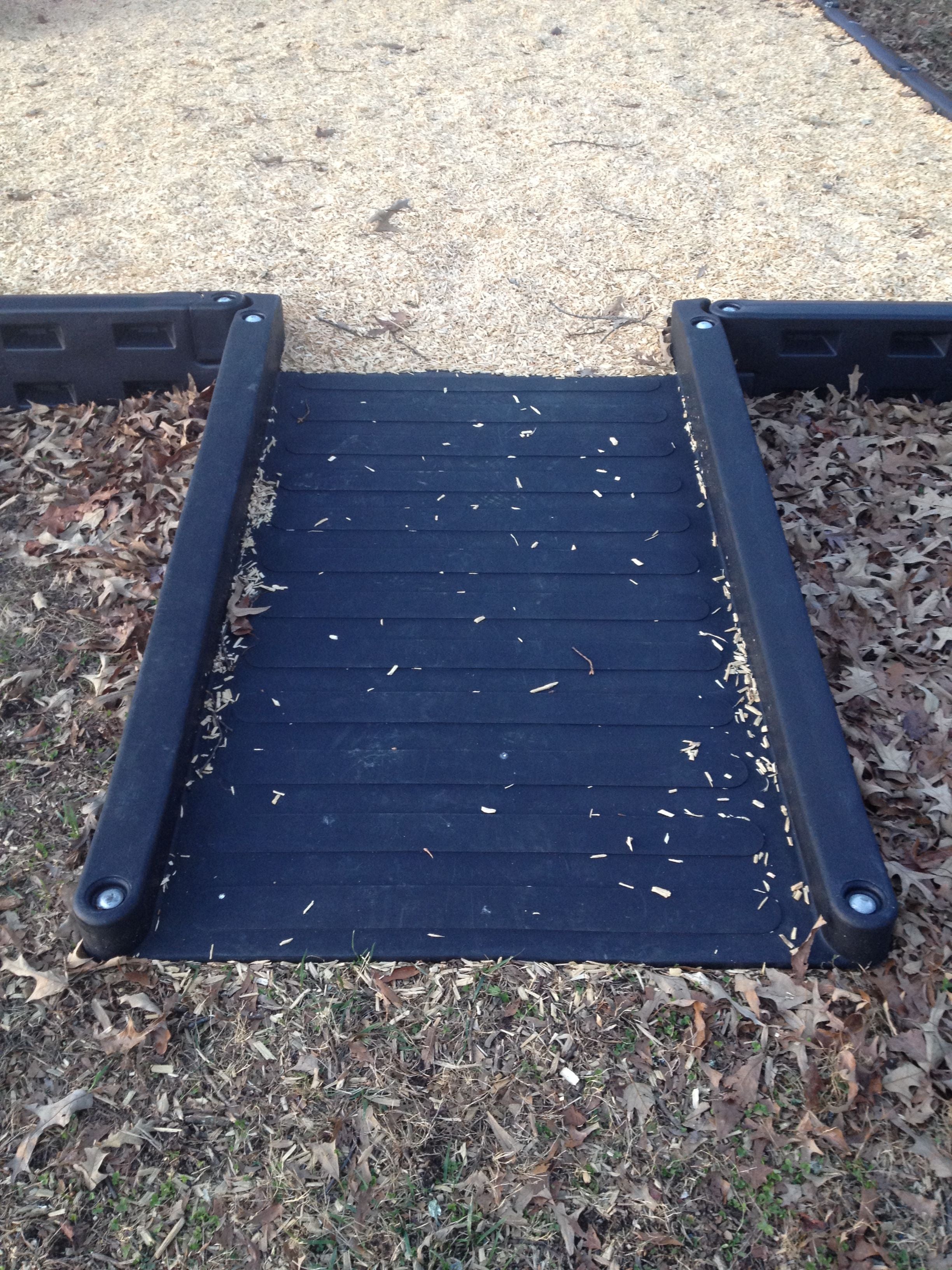 Black ADA-compliant half ramp with textured surface and side rails for wheelchair access to playground area
