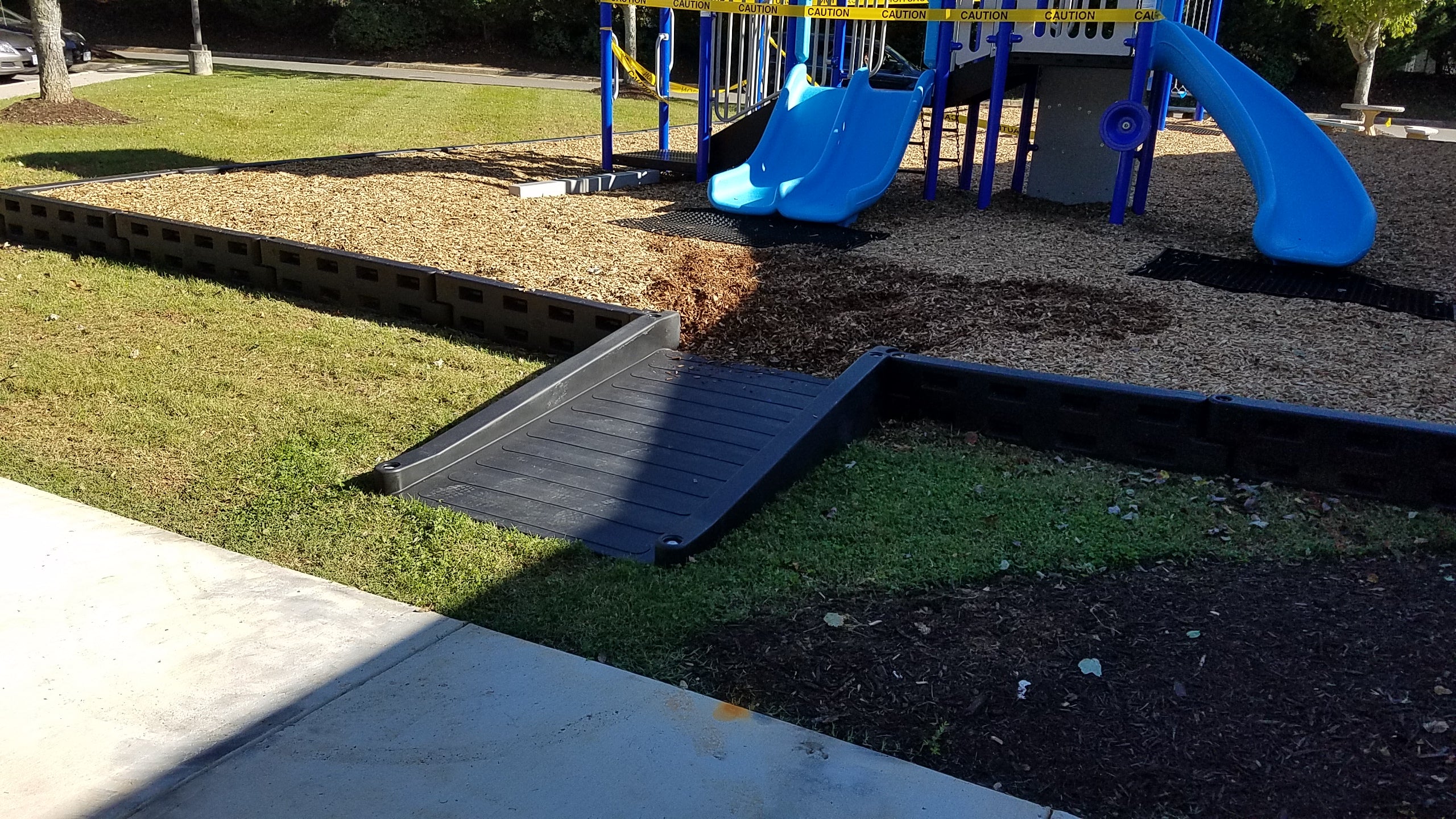 Black ADA-compliant half ramp with wheelchair access leading to playground slides and wood chip ground cover