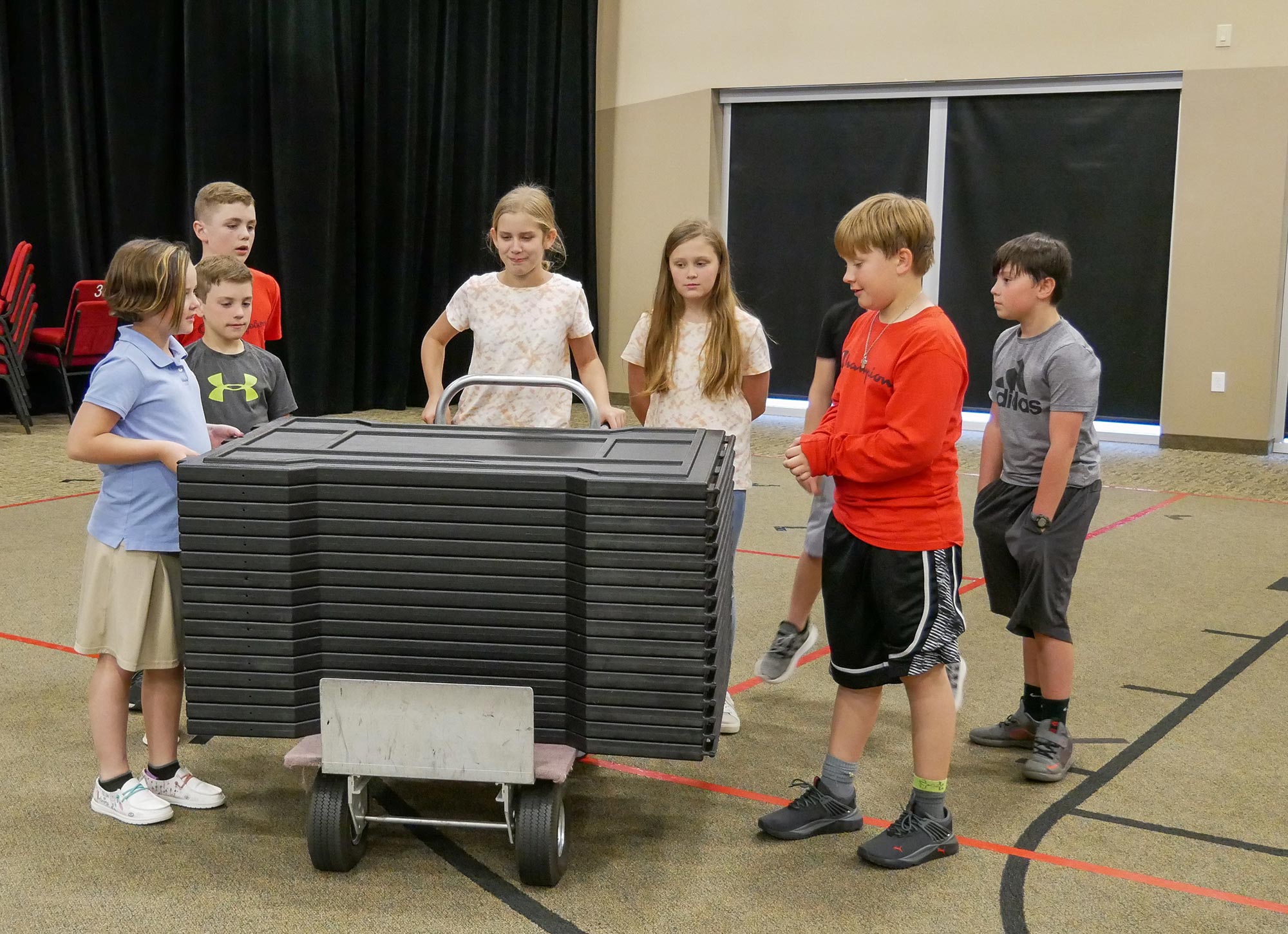 Children gathered around a stack of black portable GaGa ball pit panels indoors, ready for setup or play