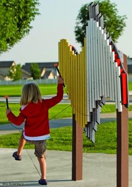 Child playing a colorful outdoor musical chime instrument with 26 anodized aluminum tubes in a park setting