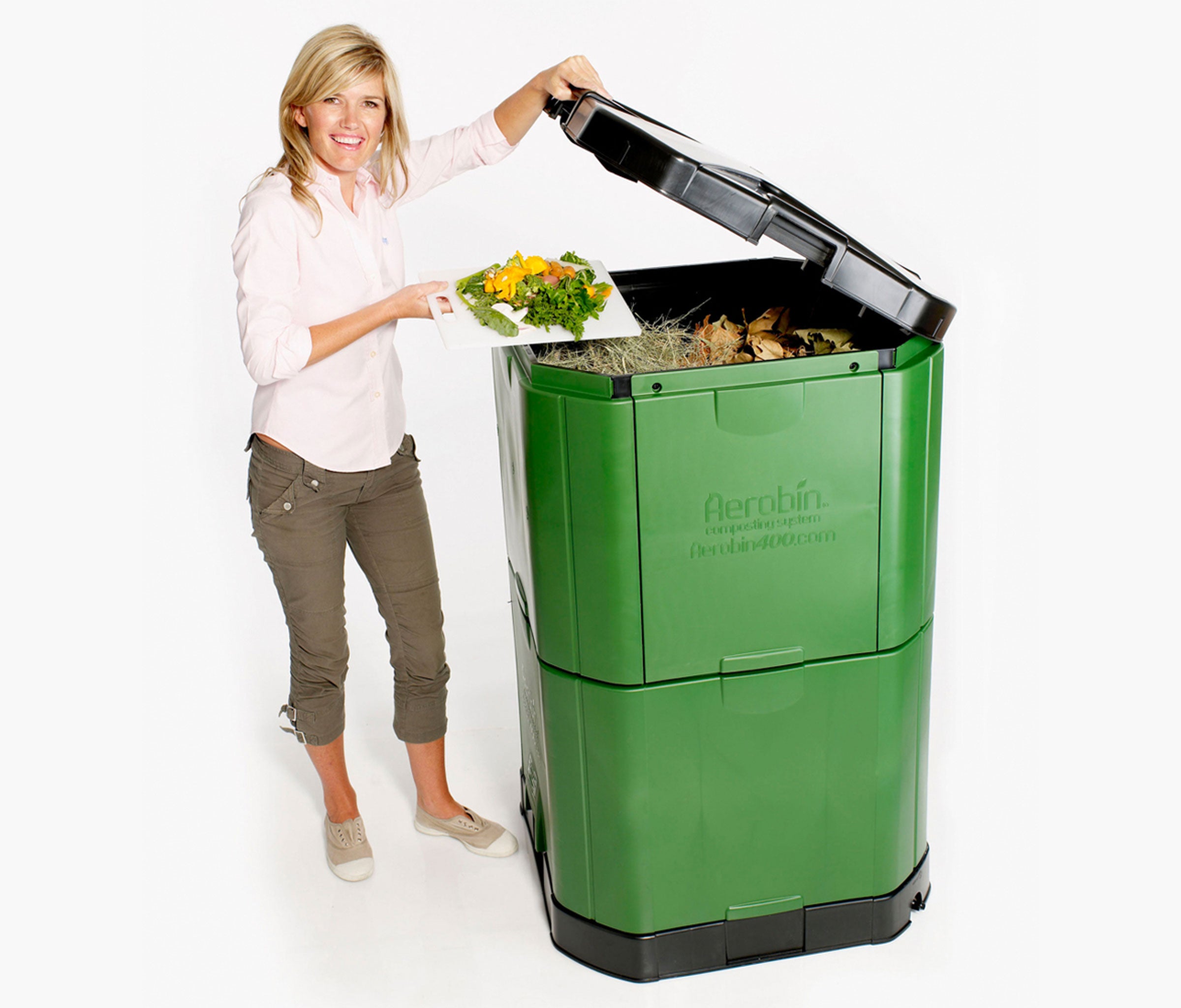 Aerobin 400 insulated compost bin with green garden waste inside, black lid open, woman adding kitchen scraps