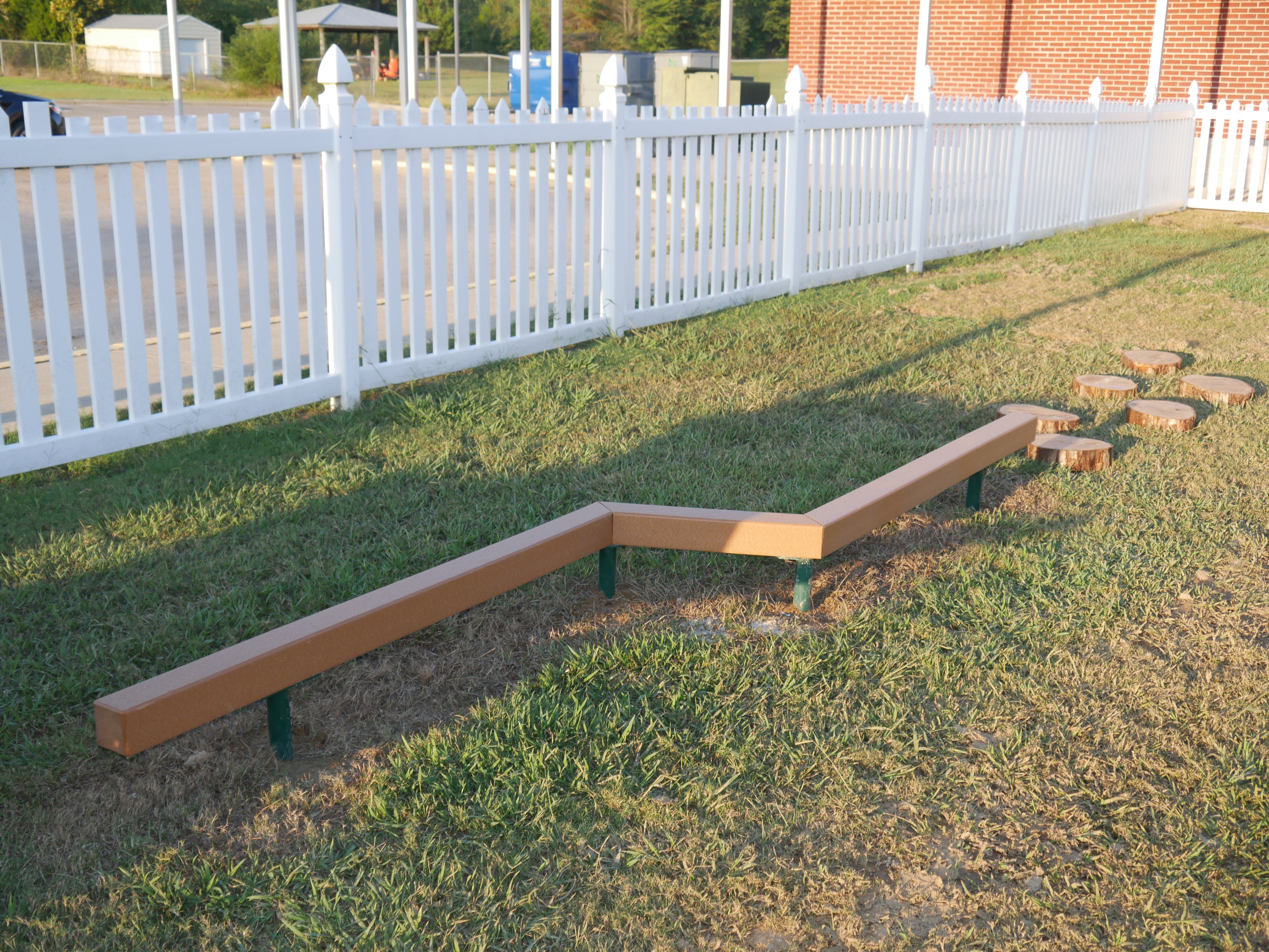 Outdoor zigzag recycled plastic balance beam with adjacent wooden stepping discs on grass surface