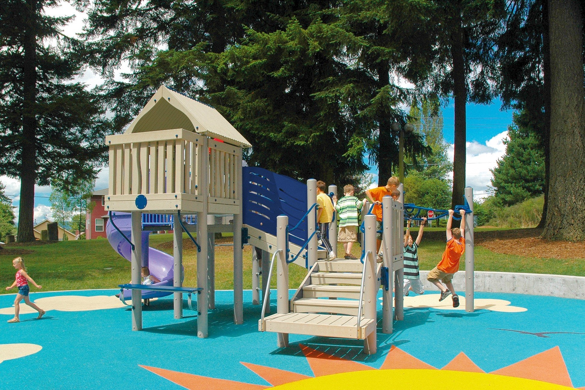 Commercial play structure with playhouse, spiral slide and overhead bars on blue safety surfacing; children in a wooded park.