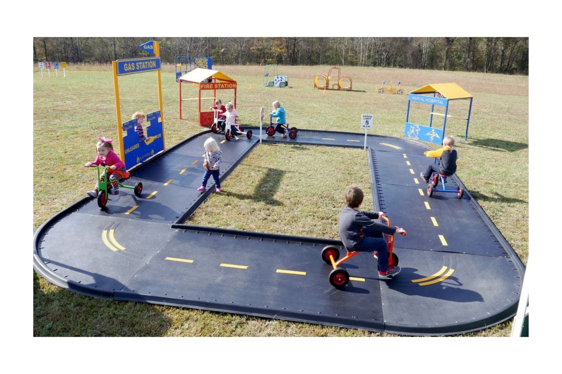 Winding outdoor trike path with black panels, yellow lane markings, traffic signs, and children riding tricycles