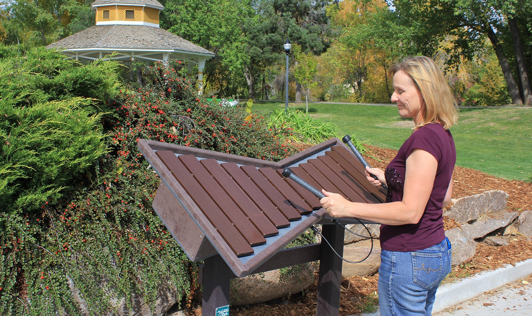 Woman playing dark brown tenor marimba with wide fiberglass keys and two mallets in an outdoor park setting