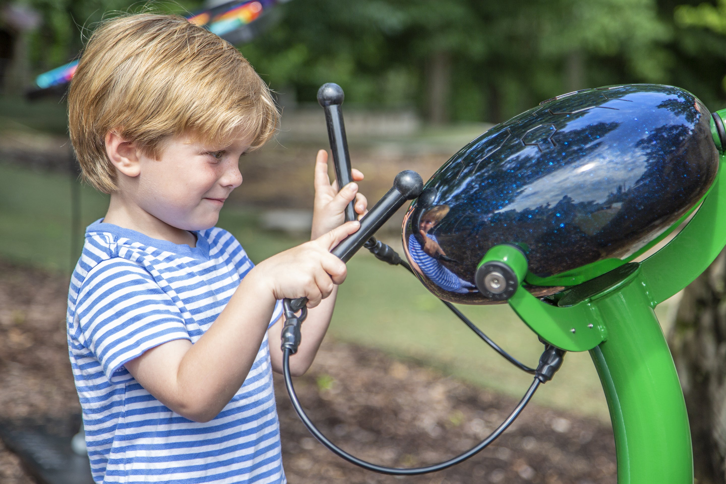 Calypso Outdoor Musical Park Instrument with black steel drum and green stand, played by child with mallets, outdoor musical equipment