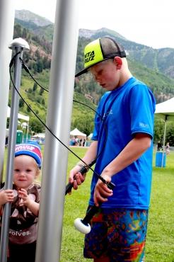 Two children playing tall outdoor contrabass chimes with mallets in a grassy park with mountains in the distance