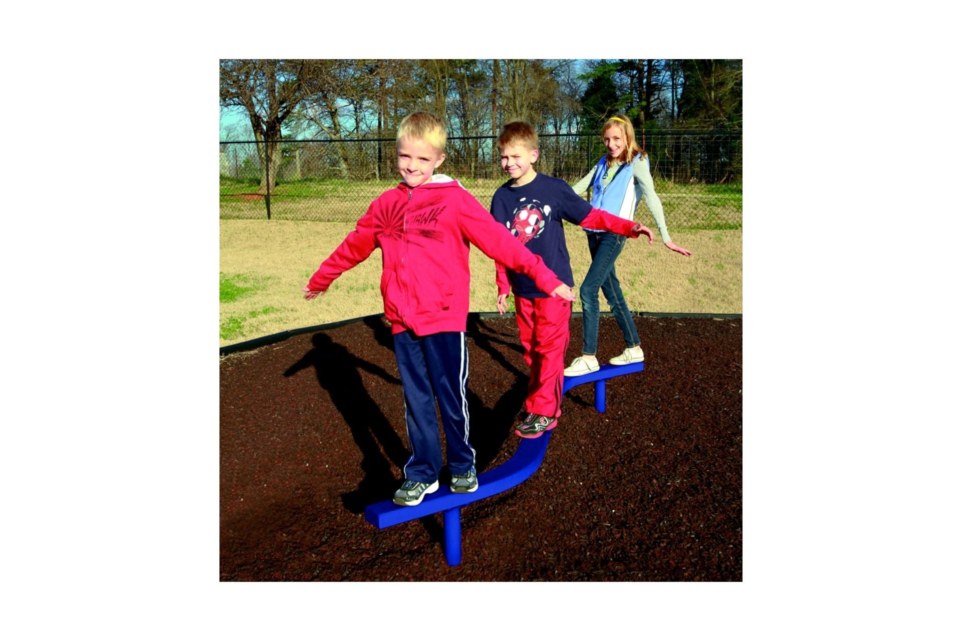 Three children balancing on a curved blue playground beam over mulch, outdoor play equipment promoting coordination and balance