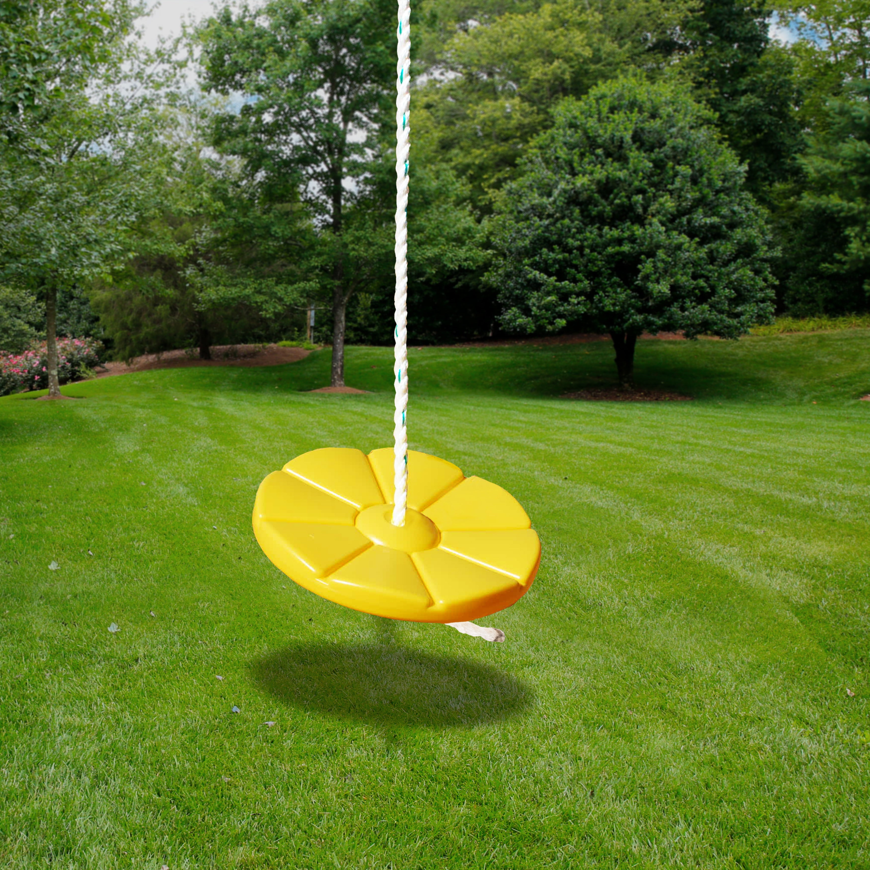 Yellow round disc swing with heavy-duty rope hanging outdoors over green grass and trees