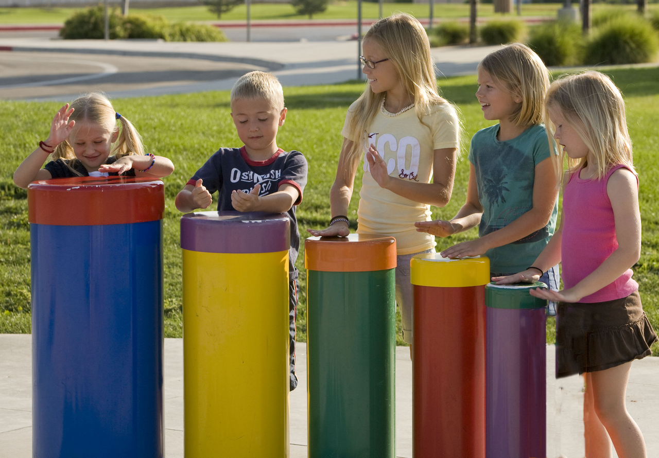 Children playing colorful outdoor percussion drums in a park setting with vibrant musical instruments