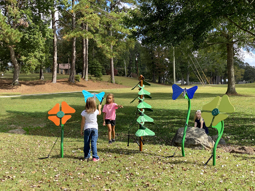 Colorful outdoor musical garden instruments shaped like flowers, butterflies, and a tree on grass with children playing nearby.
