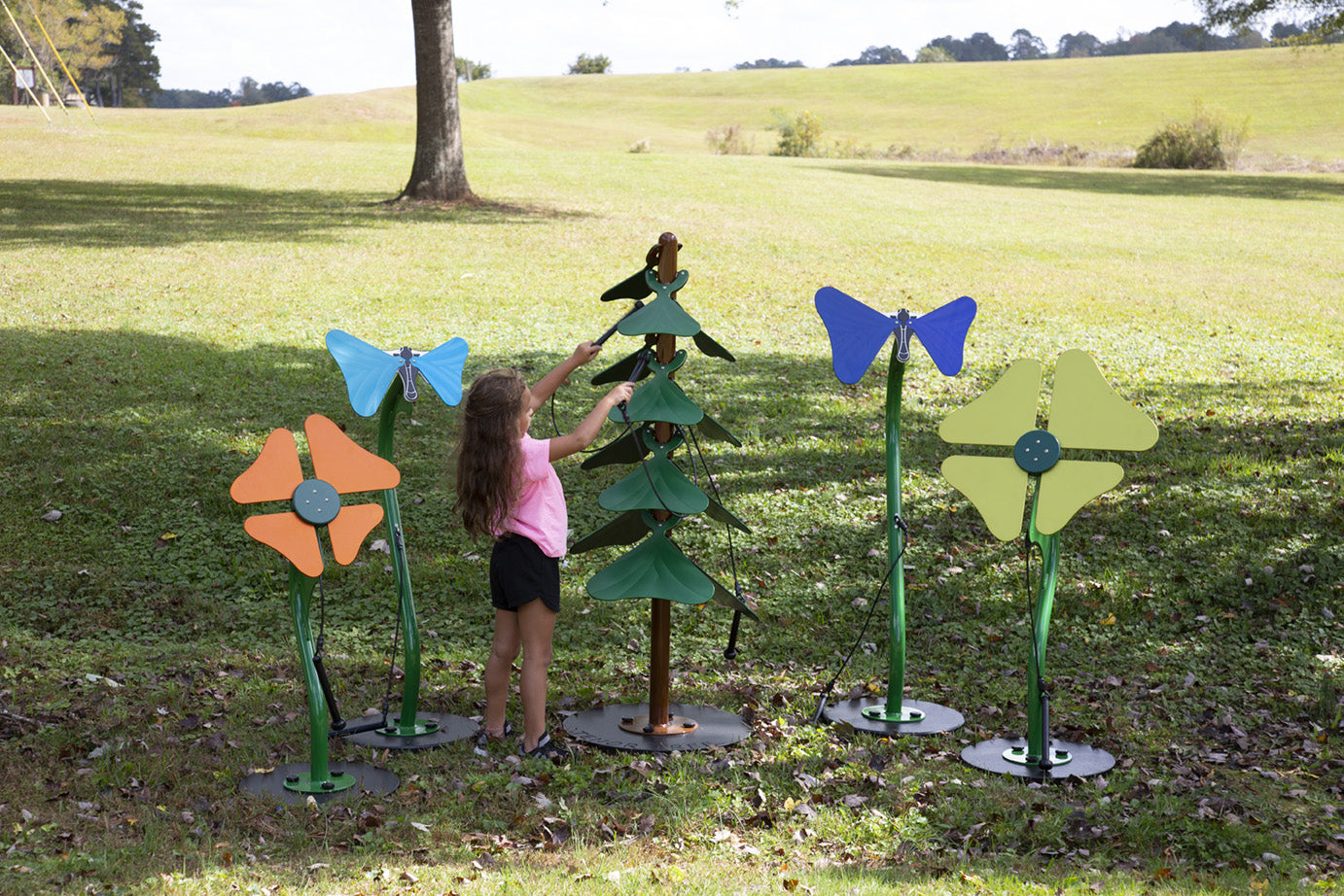 Child playing colorful outdoor musical instruments shaped like flowers, butterflies, and a tree on grass in a compact garden setting