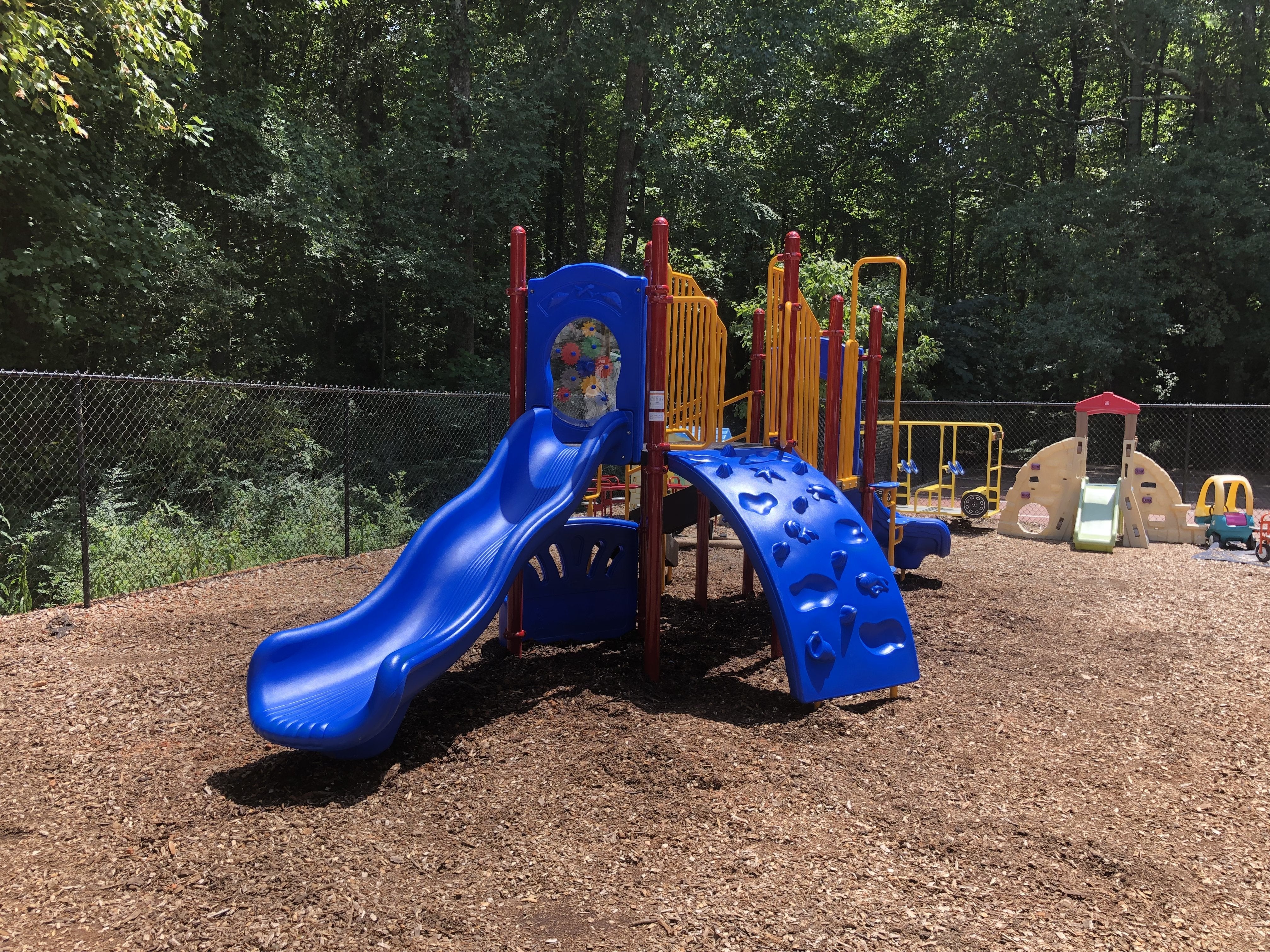 Colorful nautical-themed playground with blue wave and turn slides, seashell and starfish climbers, red and yellow railings on wood chip ground