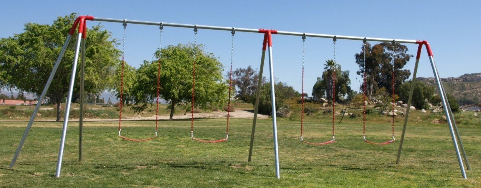 Heavy duty metal swing set with four red chain swings in a grassy park under clear sky