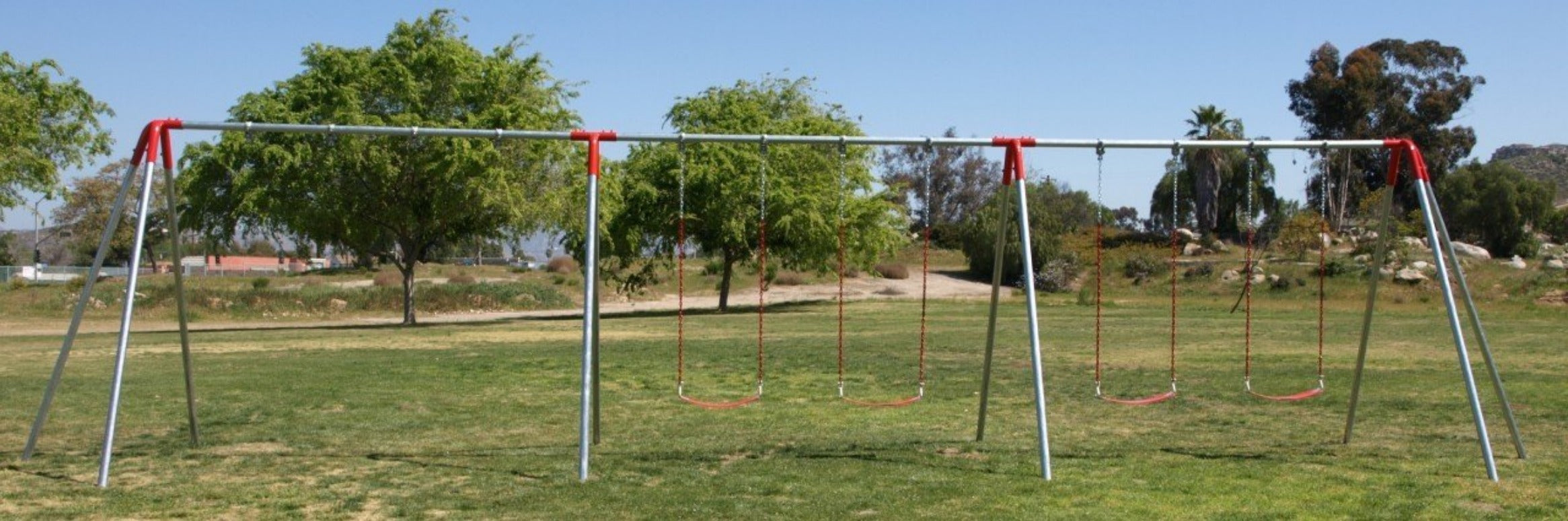 Heavy duty metal swing set with six red chain swings in a grassy park under clear sky