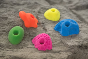 Fluorescent climbing handholds in varied shapes attached to textured outdoor climbing boulder surface