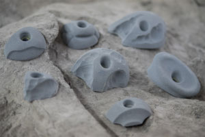 Gray climbing holds with varied shapes and holes mounted on textured rock surface for bouldering